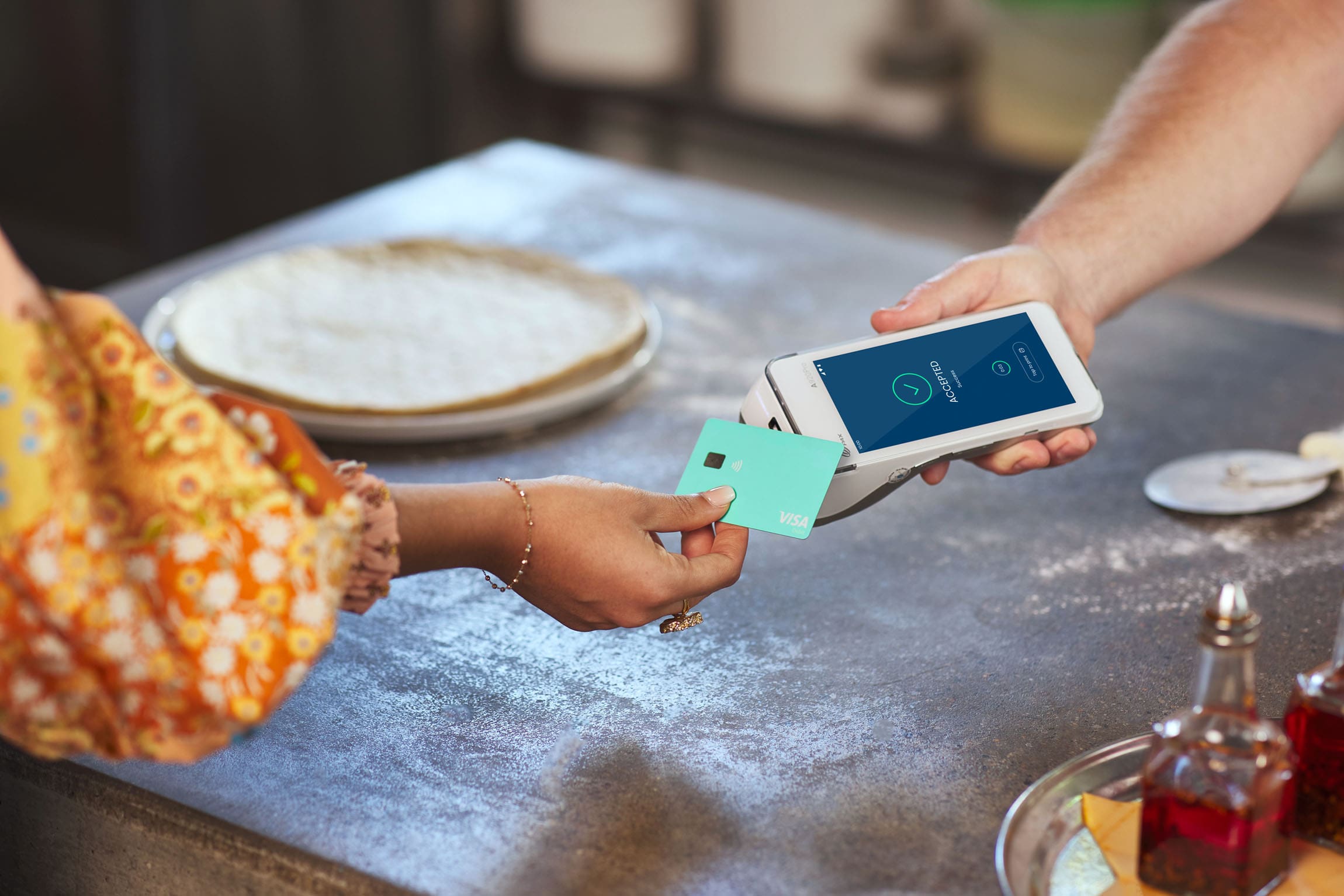 Person tapping Visa card on Android terminal with Pizza items in background