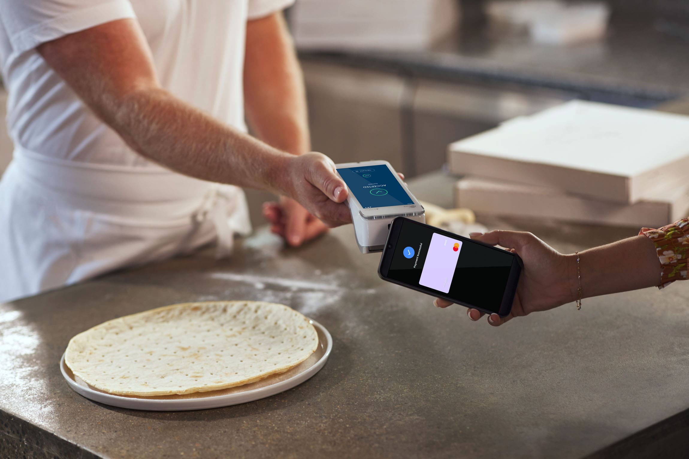 Person tapping Phone on Android terminal with Pizza items in background