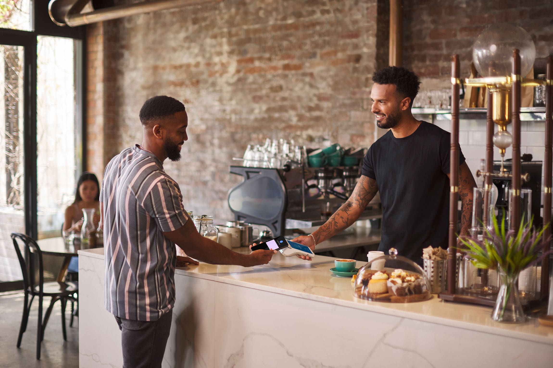 Wide shot of man tapping phone on Android terminal held by worker in a Cafe Shop