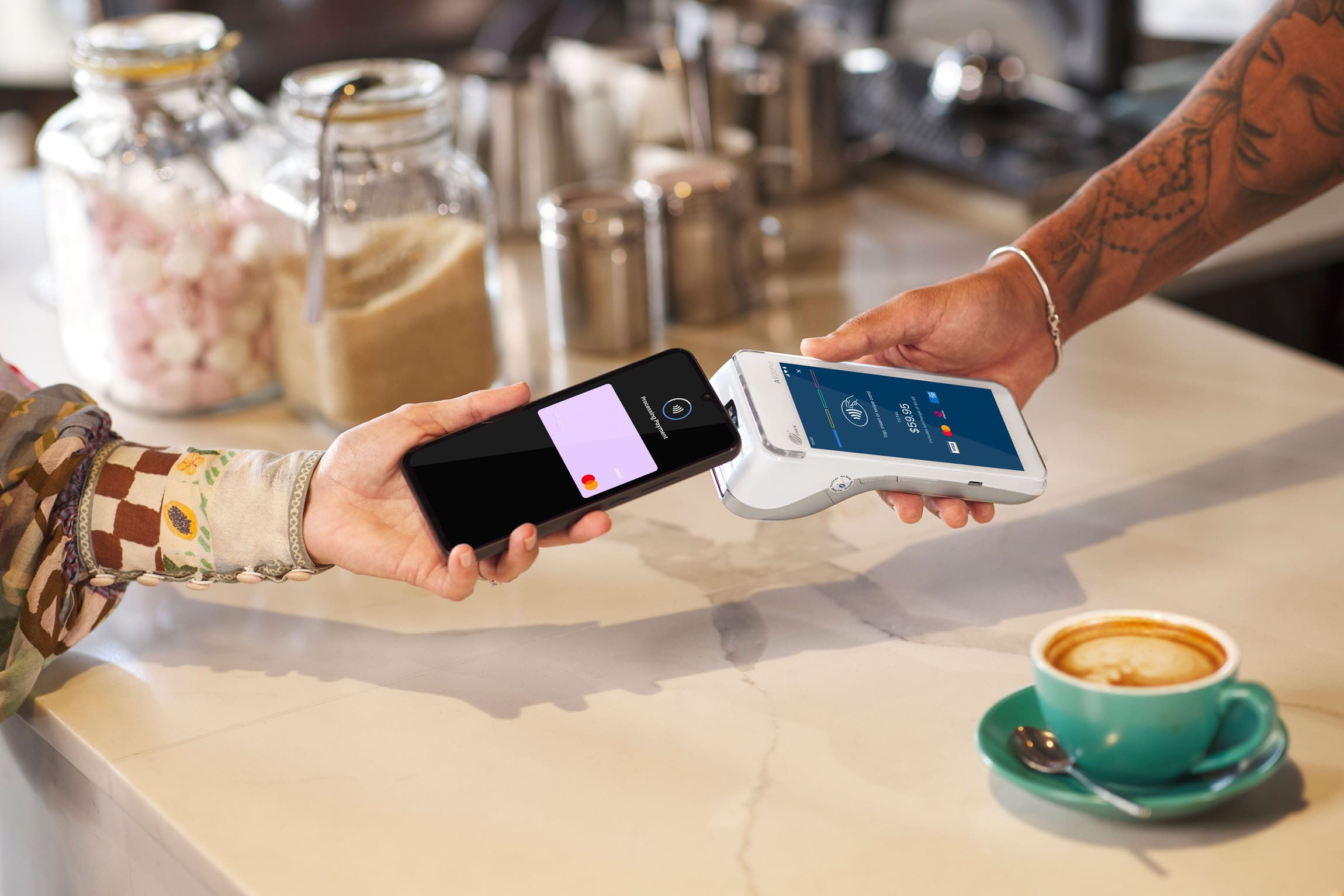 Hand holding phone tapping Android terminal surrounded by cafe items