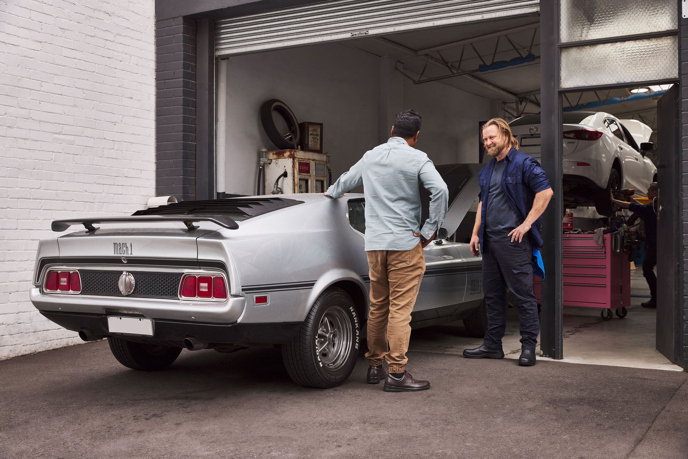 2 men facing each other holding onto car at mechanic garage