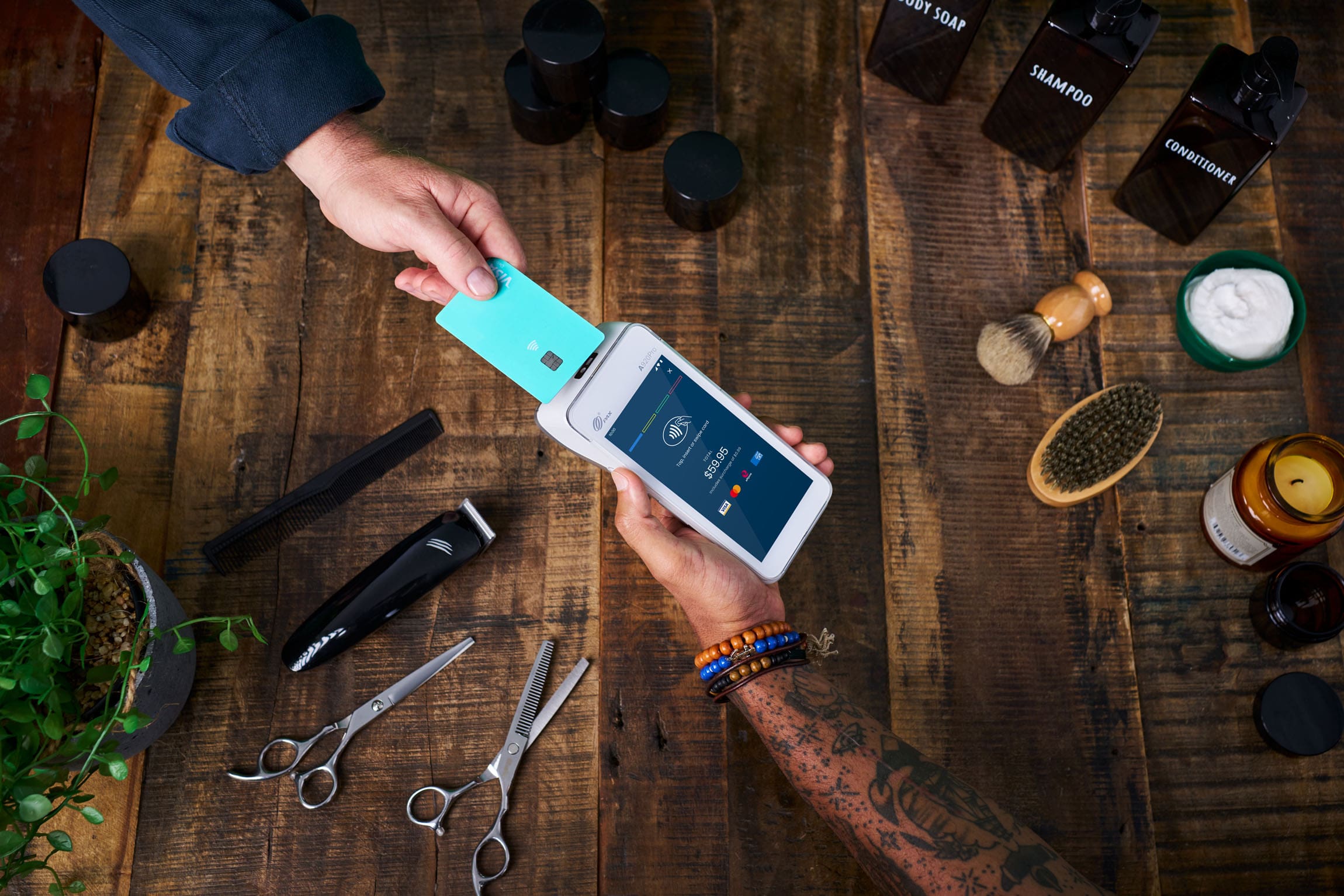 person tapping Visa card on Android terminal over wooden table surrounded by hair accessories