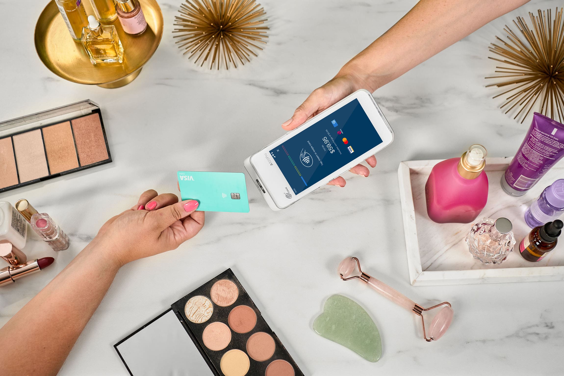 Visa card tapping Smartpay Android terminal surrounded by cosmetic accessories