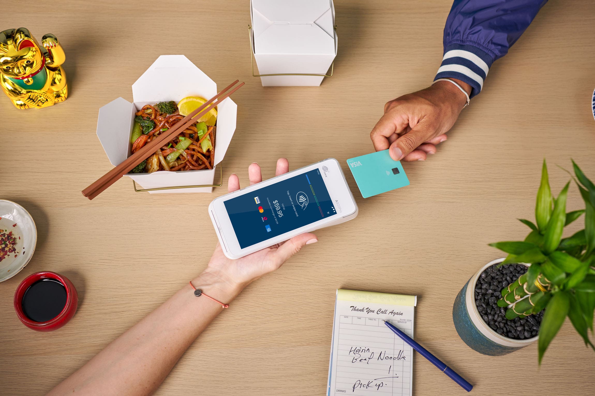 Visa card tapping Android terminal surrounded by takeaway shop items