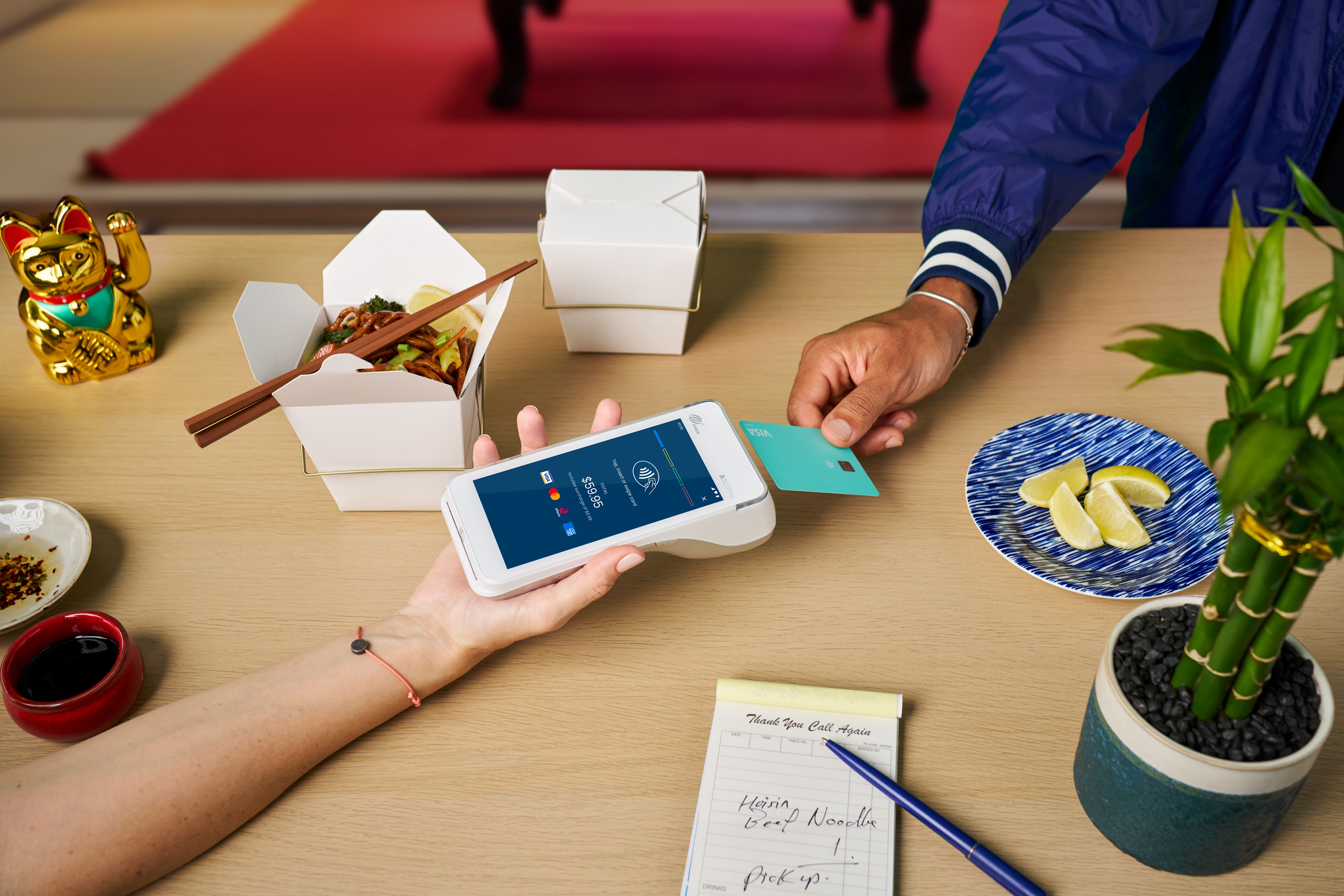 Person holding Visa card over Android terminal on table with takeaway shop items