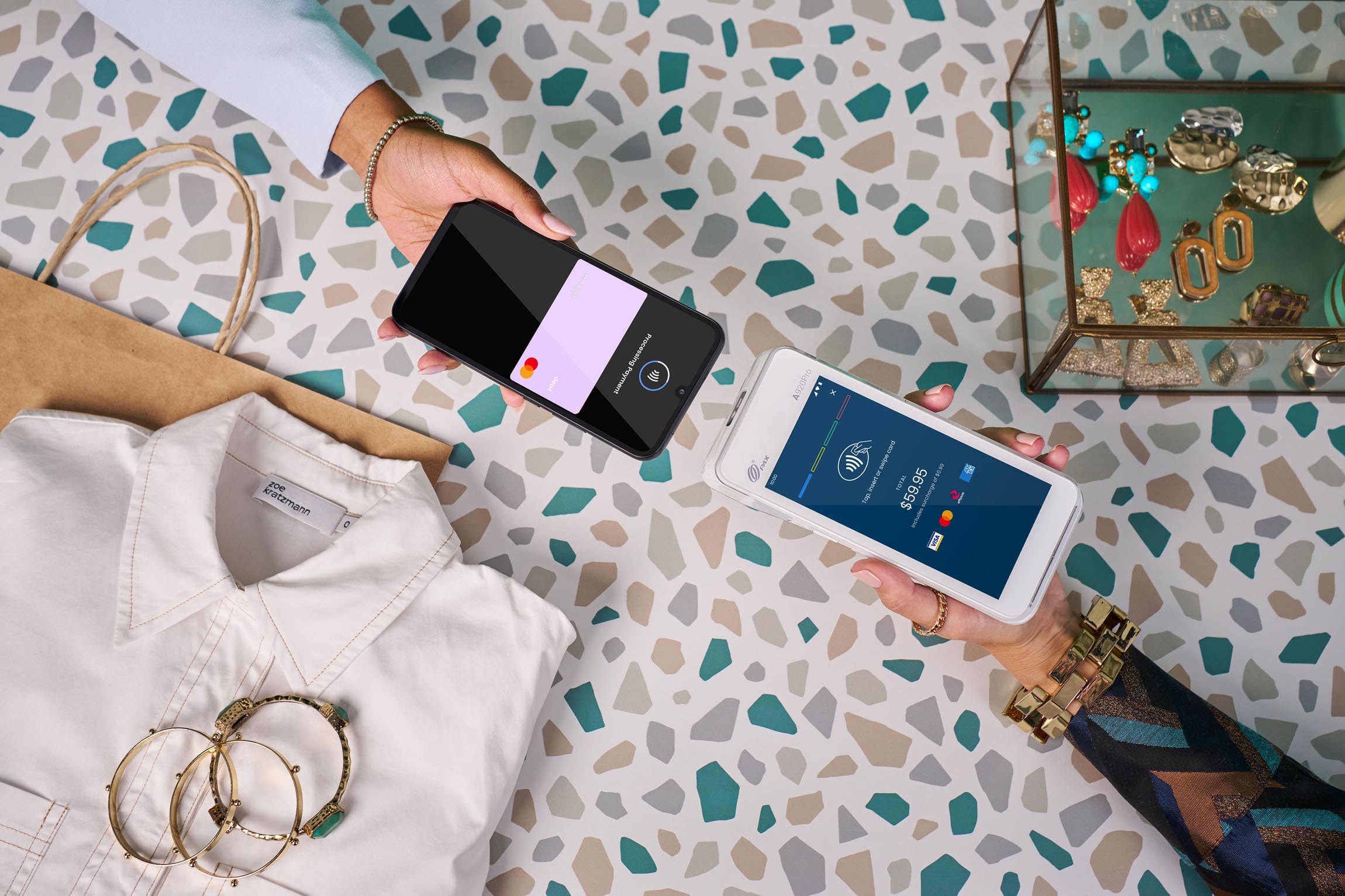 Phone tapping a Smartpay terminal over terrazzo counter with clothing and accessories around