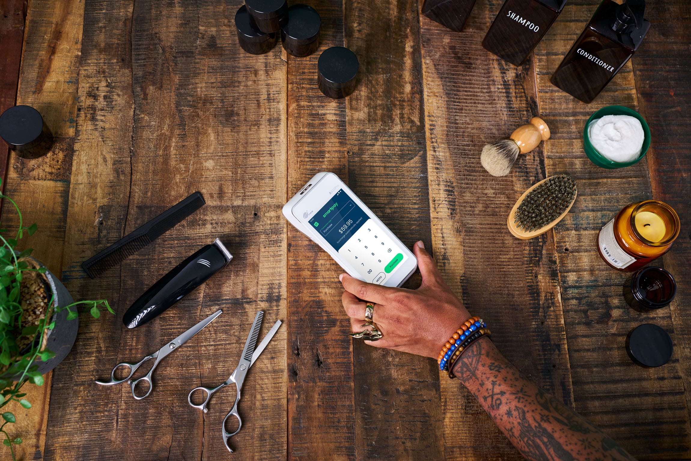 Hand holding Terminal on Wooden table surrounded by barber accessories