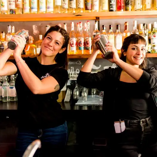 2 women holding shakers in a bar